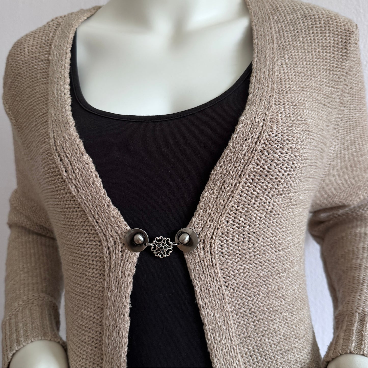 Vestsluiting Barokbloei in zachte grijstinten, gedragen op een open gebreid vest met rustige, klassieke uitstraling.