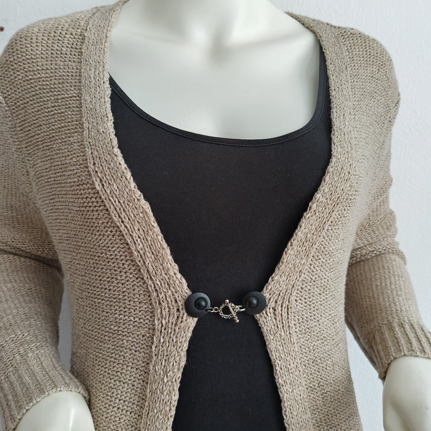 Vestsluiting met mat zwarte clips en een zilverkleurige bloemrand-bedel, handgemaakt voor een stijlvolle en subtiele afwerking.