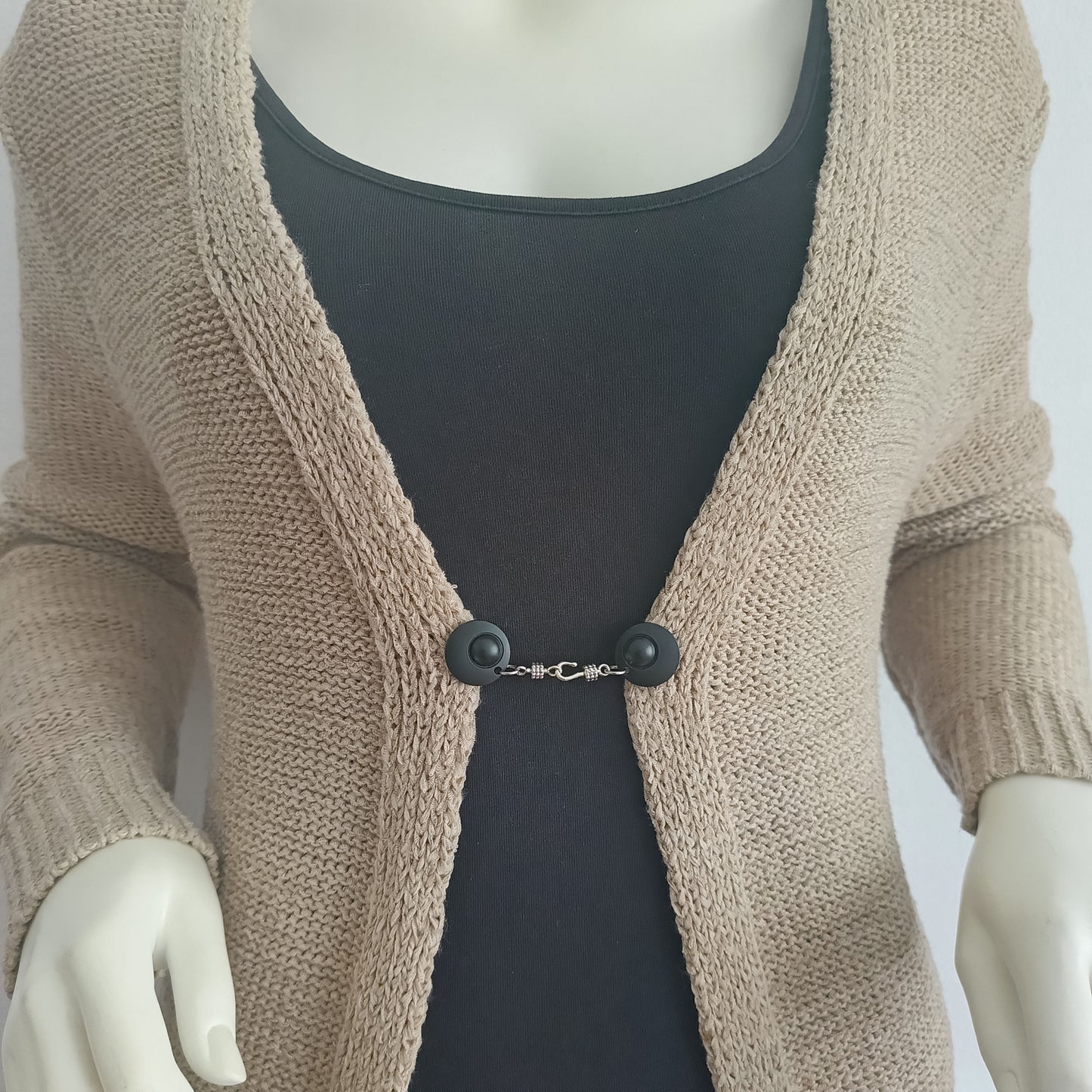 Mat zwarte vestsluiting met zilverkleurige haaksluiting, gedragen op een open gebreid vest voor een stoere uitstraling.