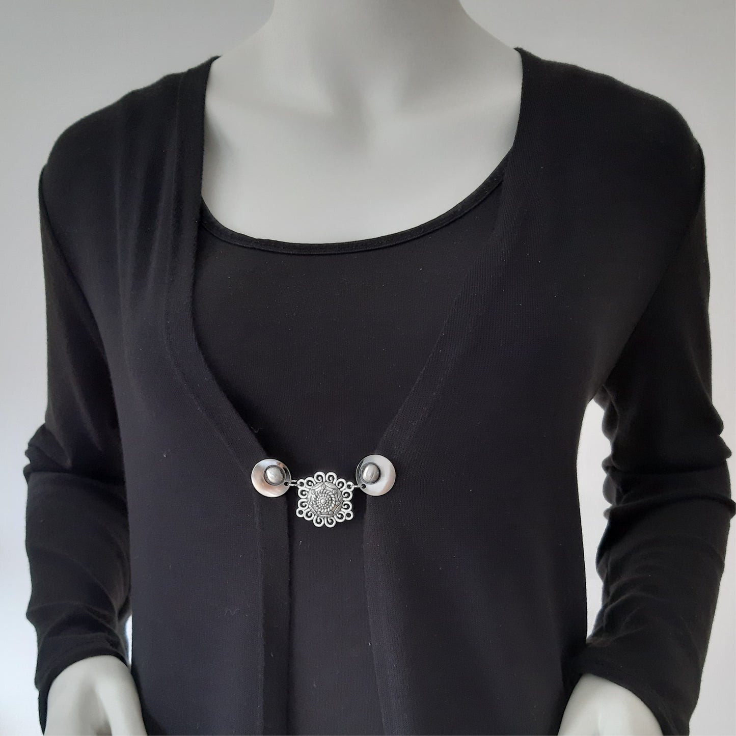 Vestsluiting De Knoopkunst gedragen op een zwart vest, elegante Fashionclip met zilverkleurige clips en sierlijke opengewerkte tussenbedel.
