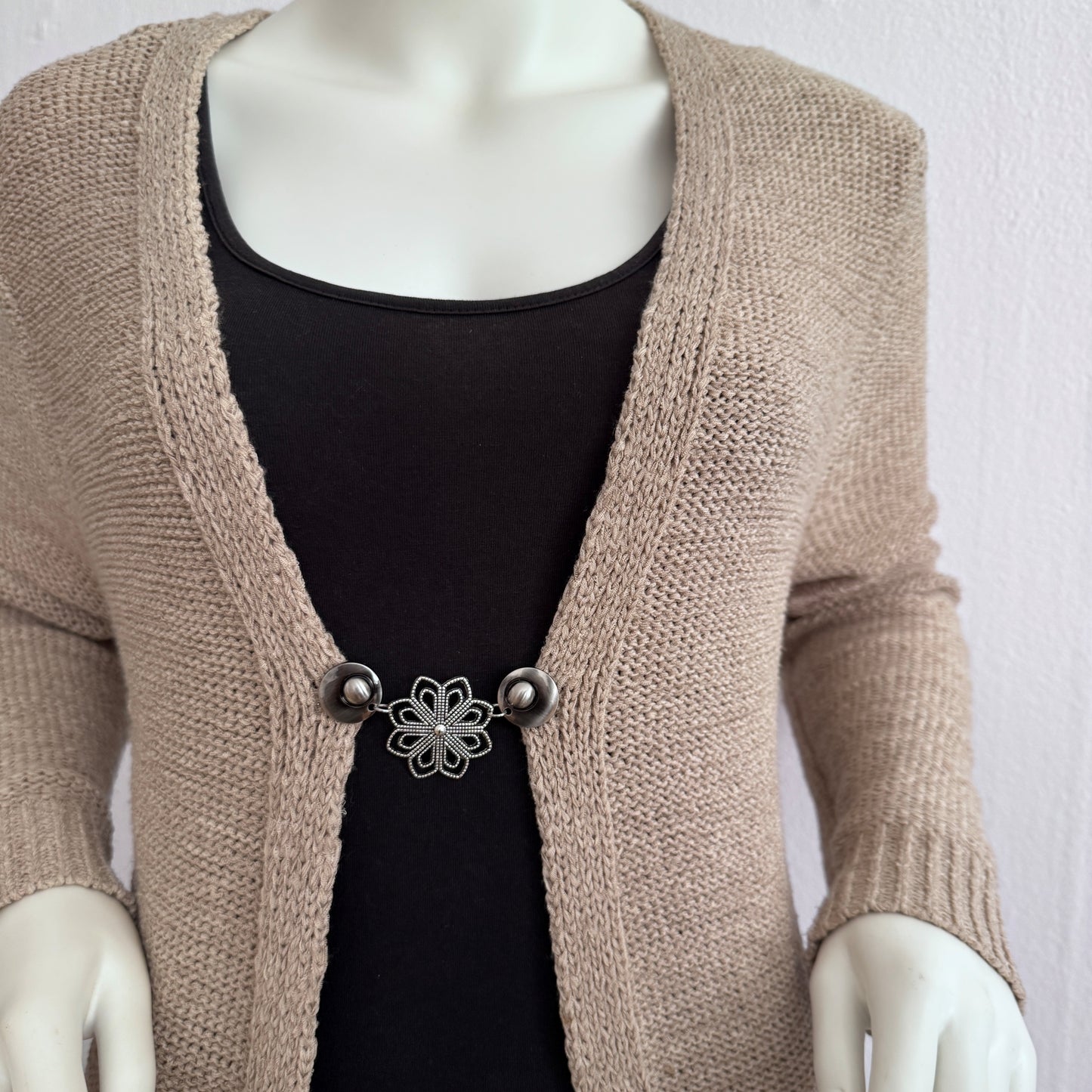 Vestsluiting De Ochtendster gedragen op een beige gebreid vest, elegante Fashionclip met zilverkleurige clips en bloemvormige tussenbedel.