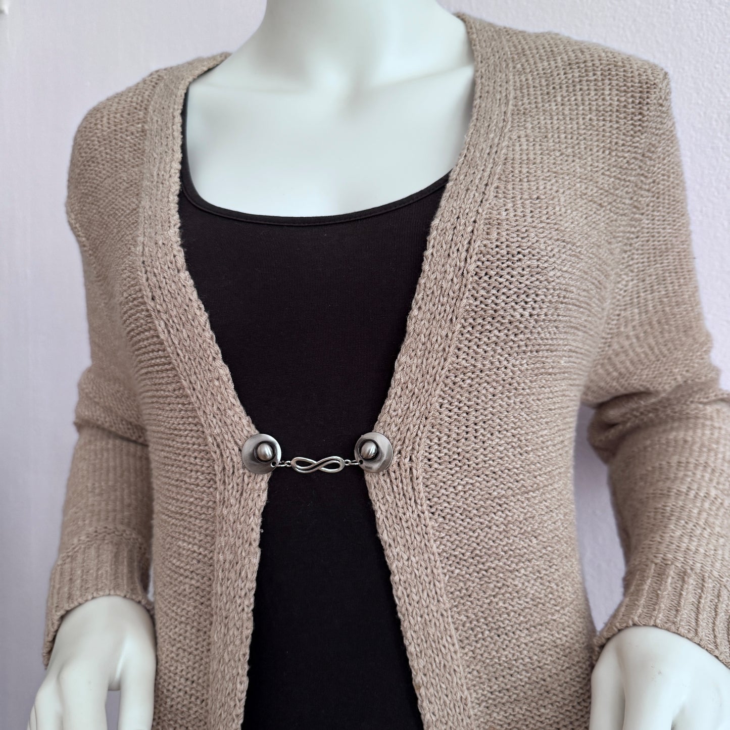 Vestsluiting De Oneindigheid gedragen op een beige gebreid vest, elegante Fashionclip met zilverkleurige clips en infinity tussenbedel.