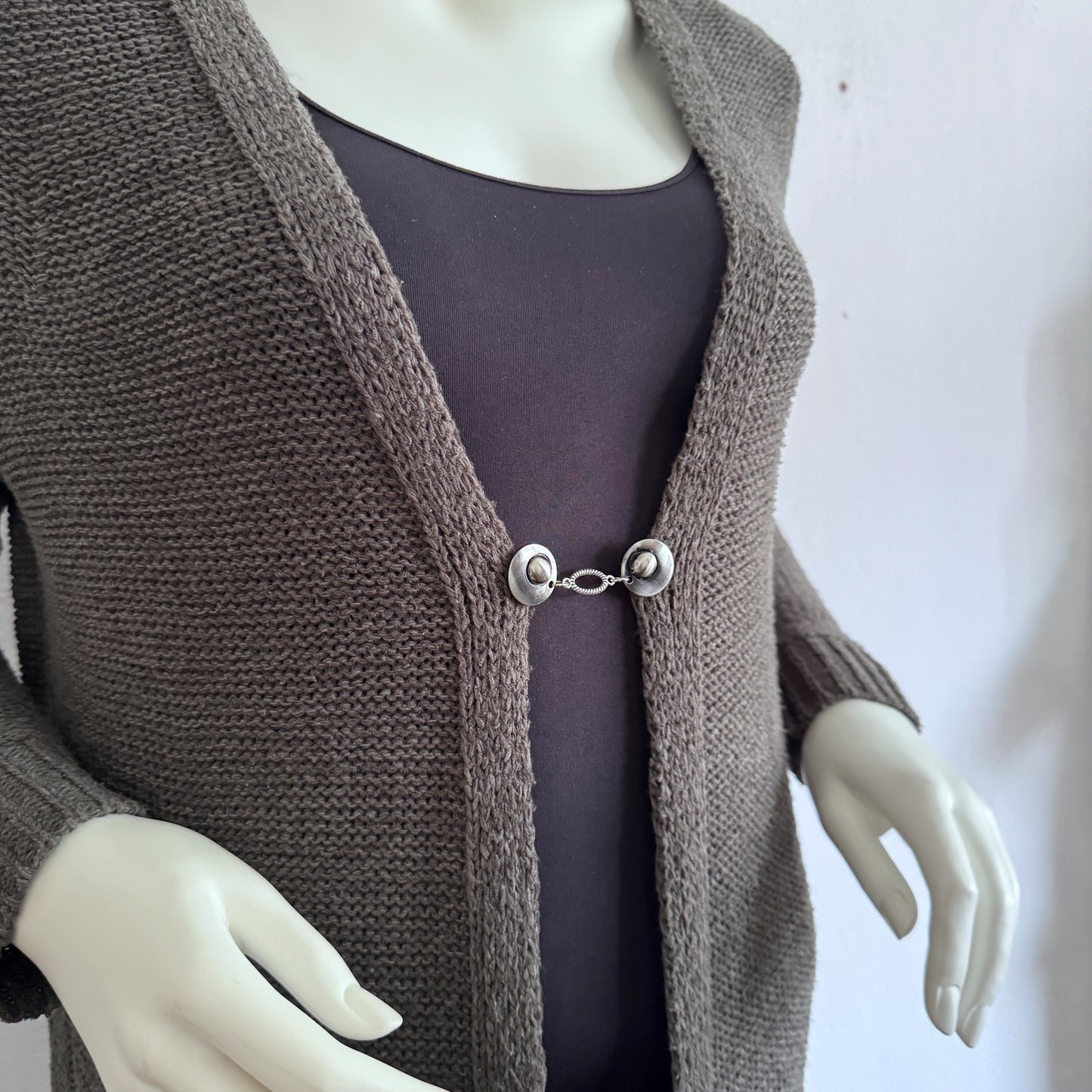 Vestsluiting De Ovaal gedragen op een taupekleurig gebreid vest, elegante Fashionclip met zilverkleurige clips en ovale tussenbedel.