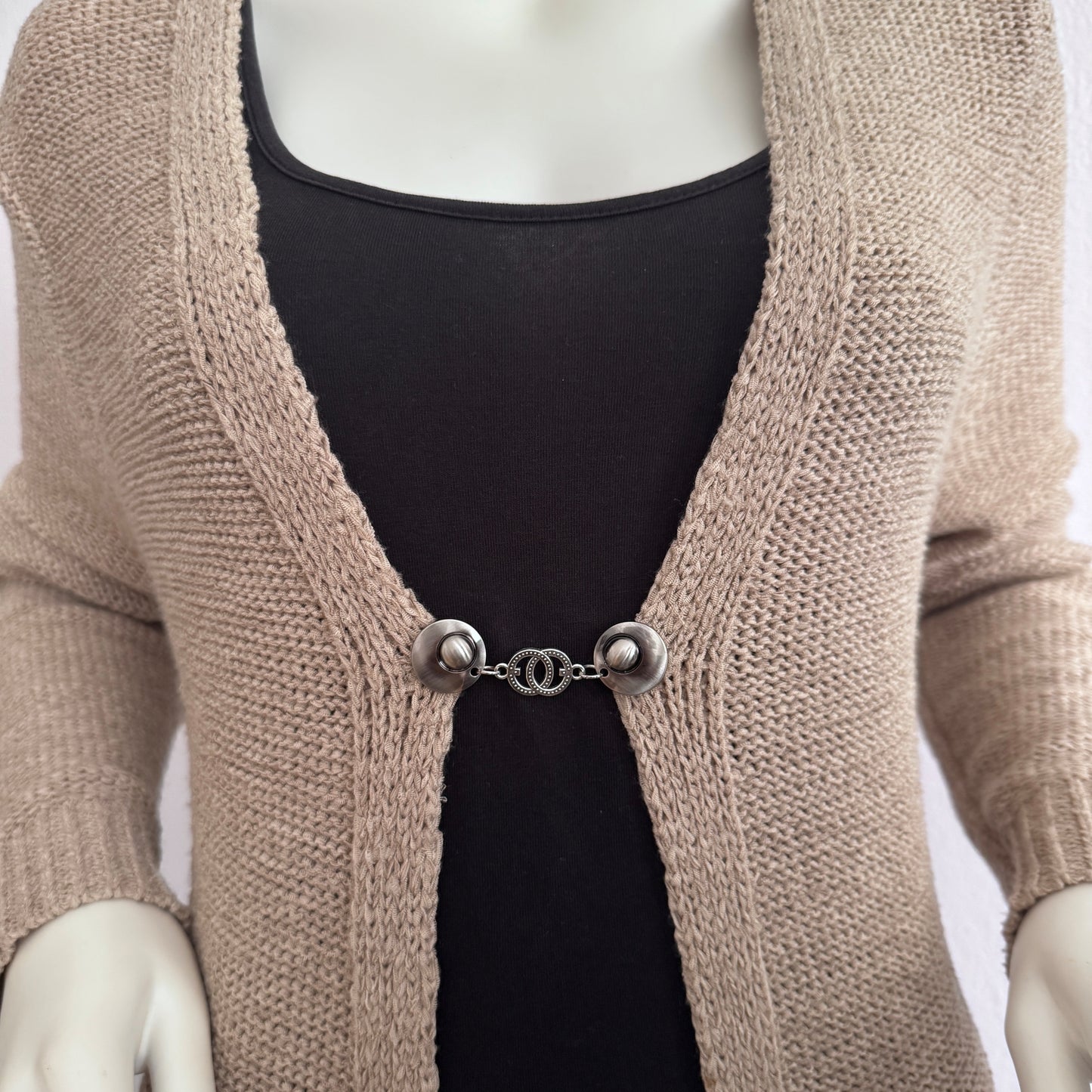 Vestsluiting De Verbinding gedragen op een beige gebreid vest, elegante Fashionclip met zilverkleurige clips en verbonden cirkelvormige tussenbedel.