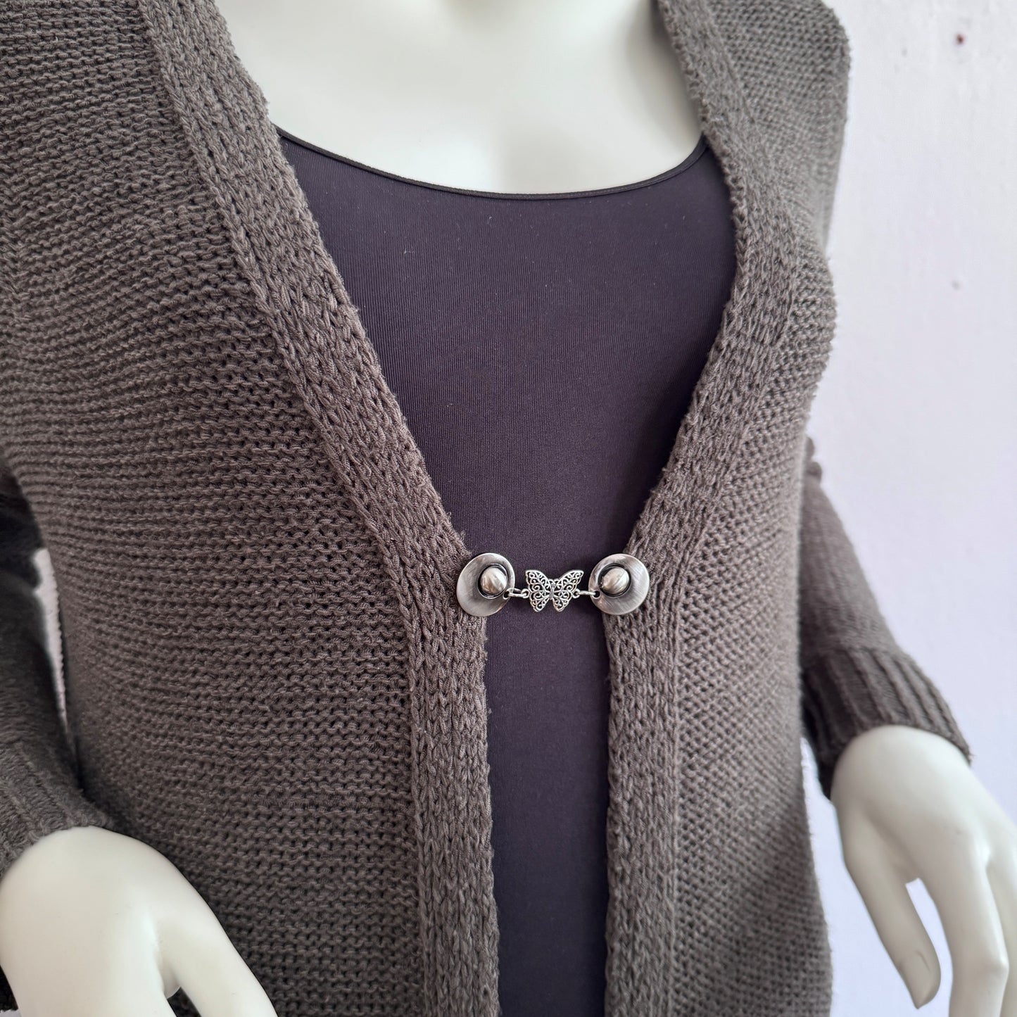 Vestsluiting De Vlinder gedragen op een taupekleurig gebreid vest, elegante Fashionclip met zilverkleurige clips en vlindervormige tussenbedel.