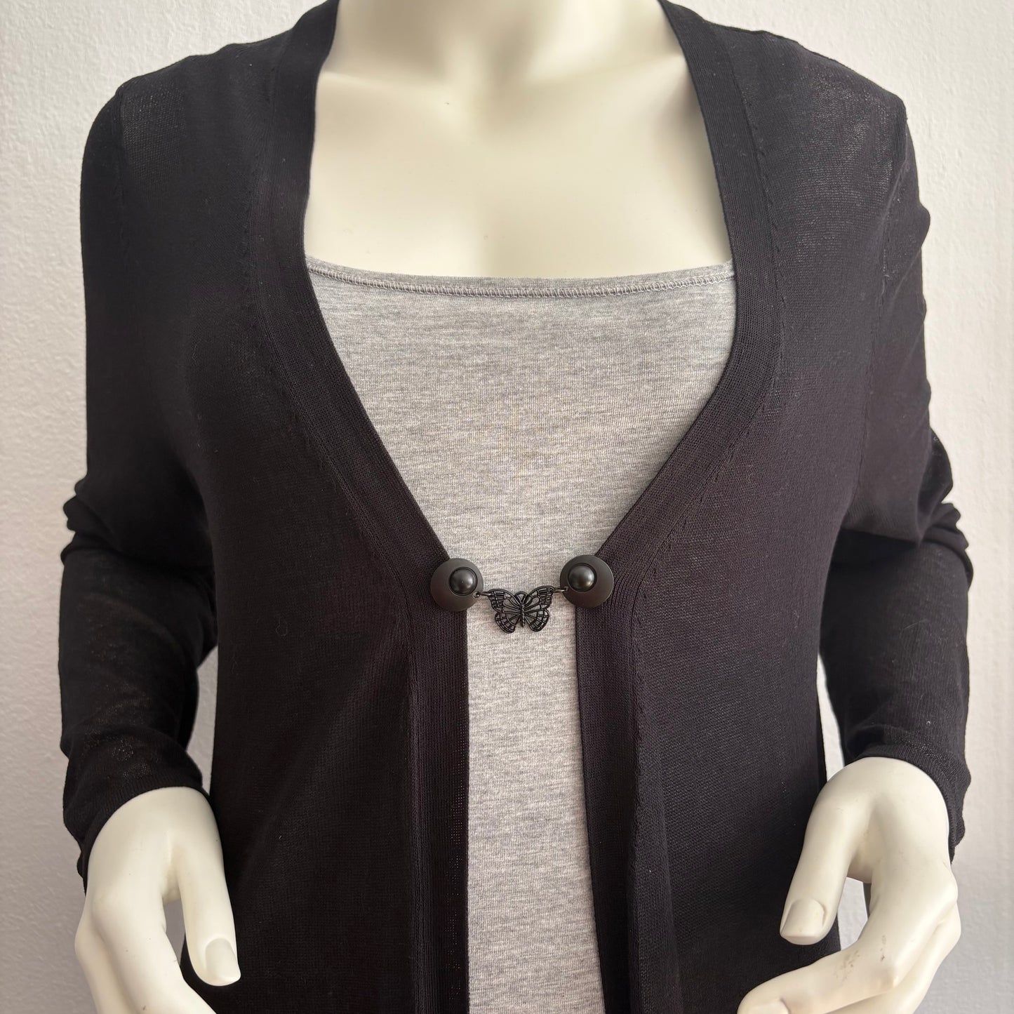 Vestsluiting De Zwarte Vlinder gedragen op een zwart vest met grijze top, elegante Fashionclip met matzwarte clips en vlindervormige tussenbedel.