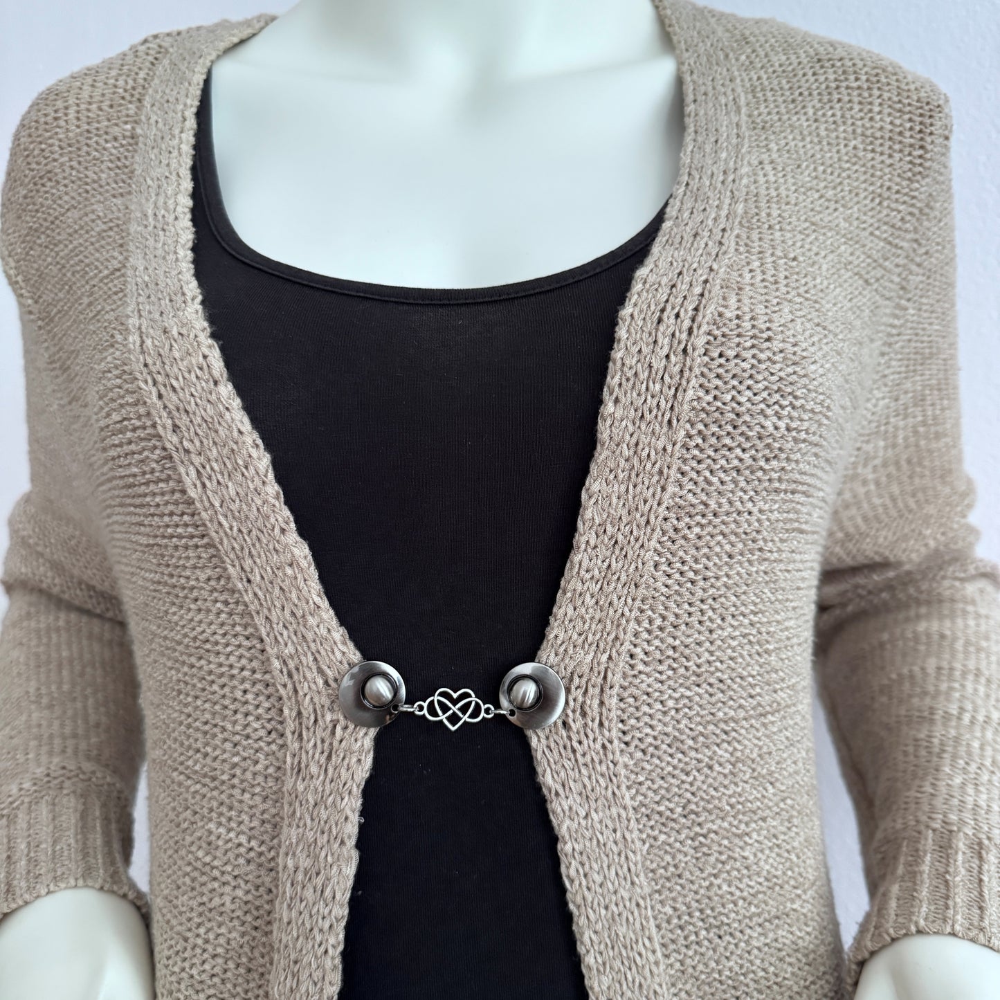 Vestsluiting Het Hart gedragen op een beige gebreid vest, elegante Fashionclip met zilverkleurige clips en hartvormige tussenbedel.