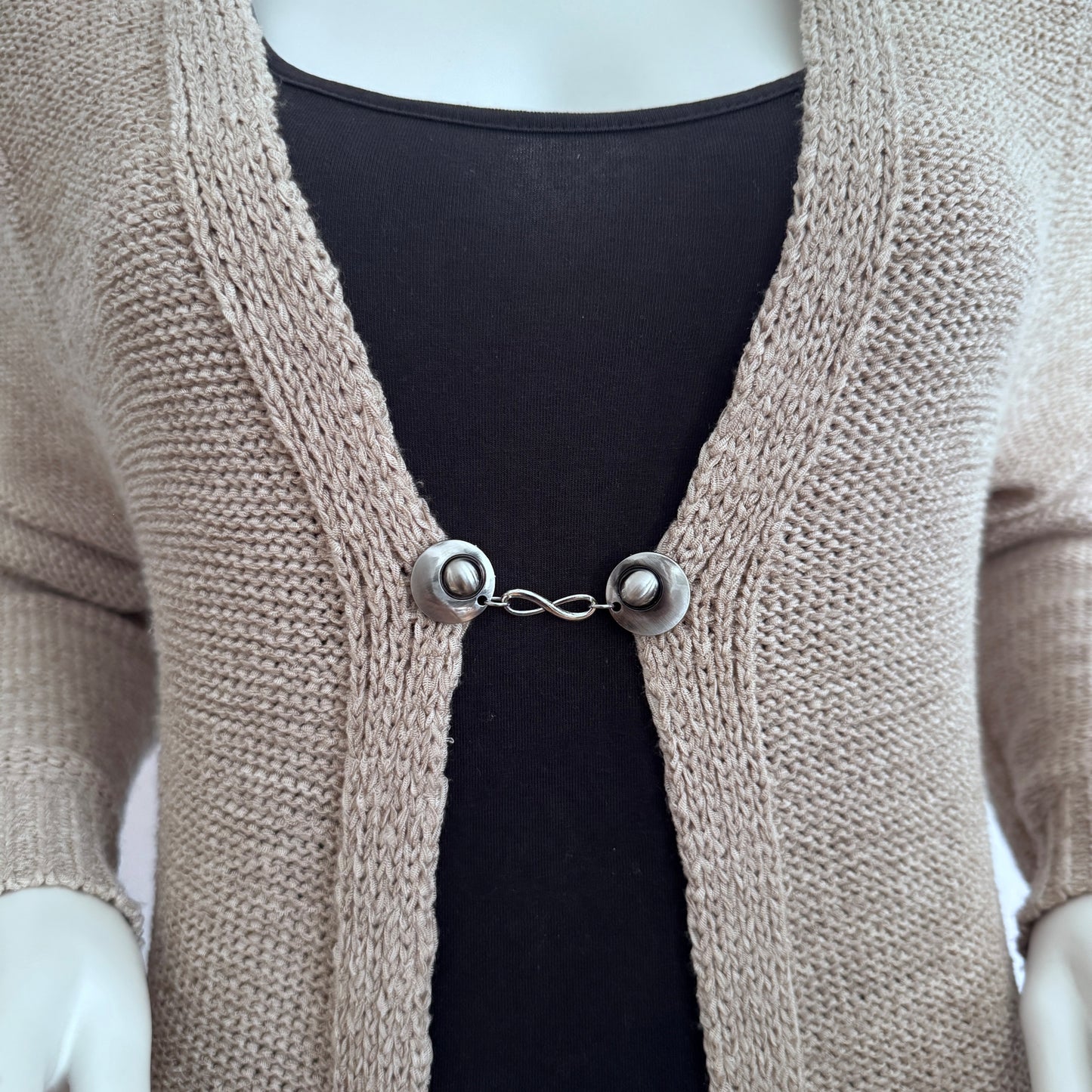 Vestsluiting Infinity zilver gedragen op een beige gebreid vest, elegante Fashionclip met zilverkleurige clips en infinity tussenbedel.