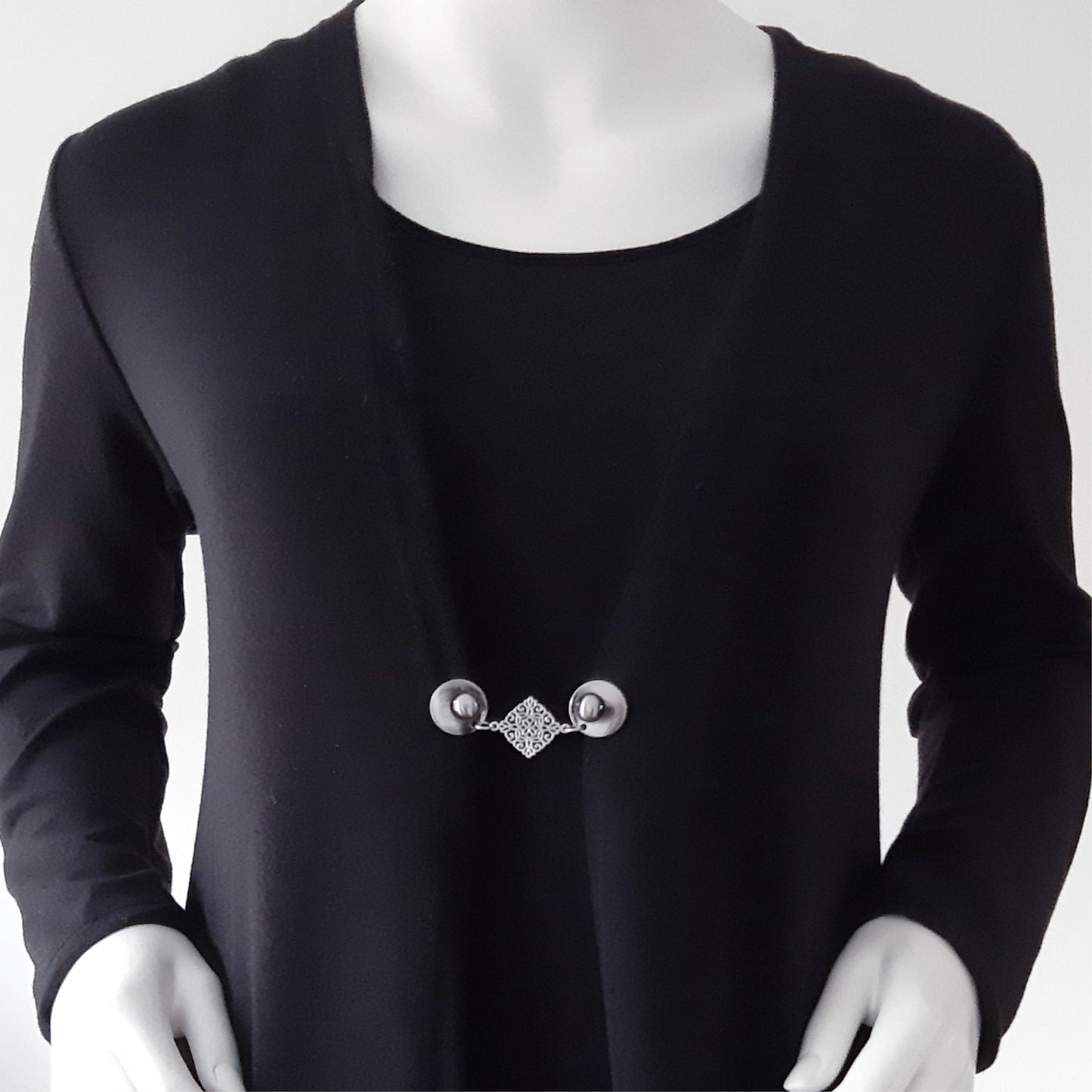 Vestsluiting met zilverkleurige clips en sierlijke ruitvormige tussenbedel, elegante Fashionclip gedragen op een zwart vest.