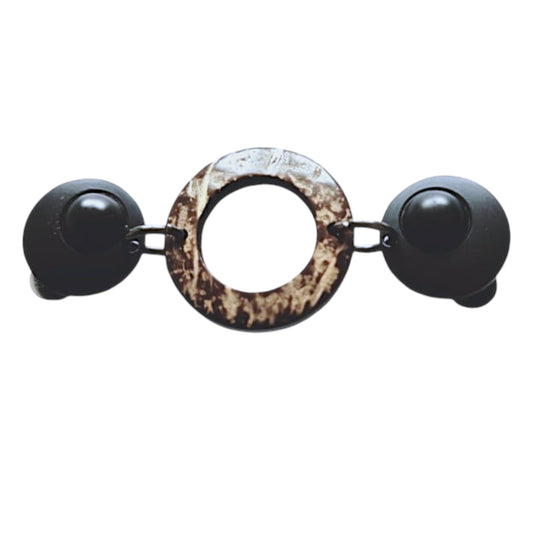 Natuurlijke vestsluiting met matzwarte clips en een ronde kokosnootschakel, voor een stoere en warme uitstraling.