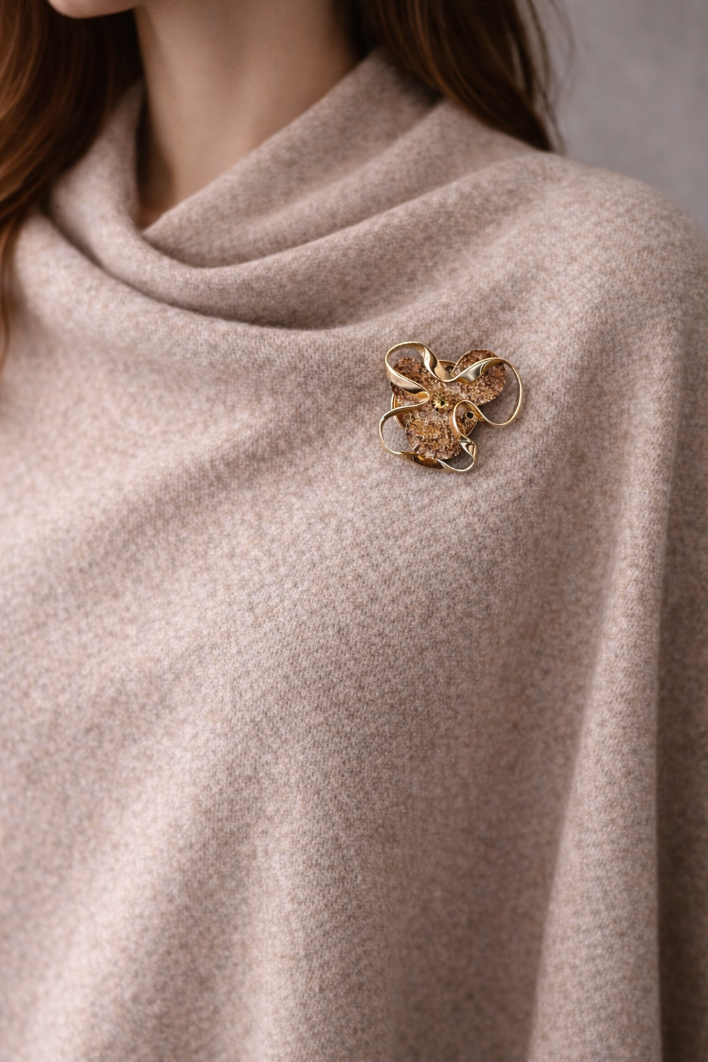 Goudkleurige magneetbroche met ronde vormen en structuur, gestyled op een zachte beige poncho