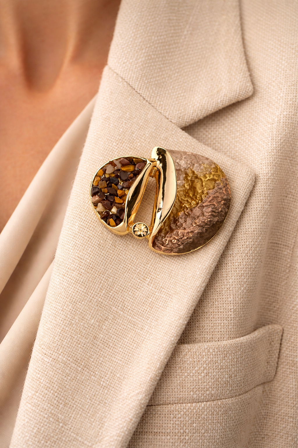 Stijlvolle magneetbroche in goudbruine tinten met glans, steentjes en reliëf, gedragen op een beige blazer