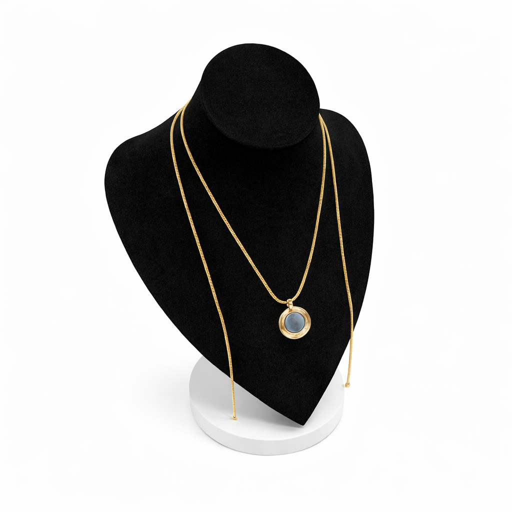 Goudkleurige magneetketting met ronde hanger, gepresenteerd op een zwart display met witte voet