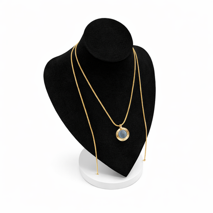 Goudkleurige magneetketting met ronde hanger, gepresenteerd op een zwart display met witte voet