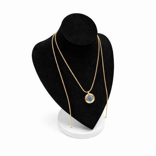 Goudkleurige magneetketting met ronde hanger, gepresenteerd op een zwart display met witte voet