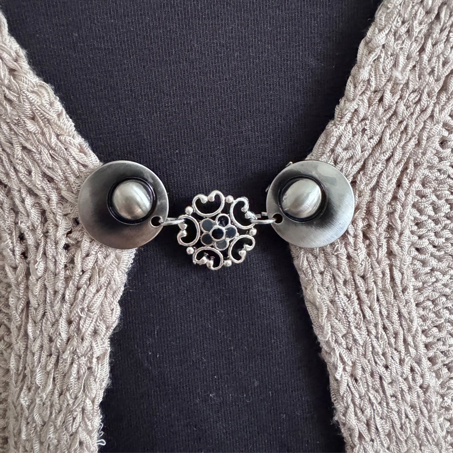 Vestsluiting Barokbloei in grijstinten met sierlijke opengewerkte bloem, gedragen op een open gebreid vest.