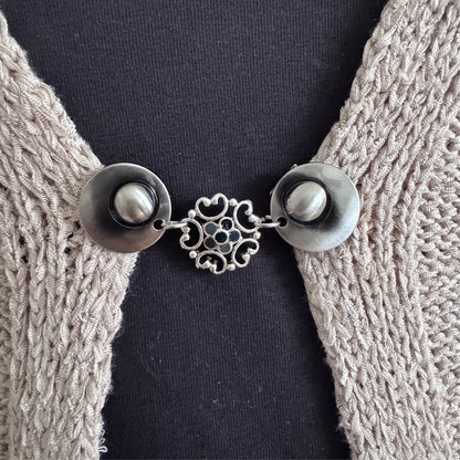 Vestsluiting Barokbloei in grijstinten met sierlijke opengewerkte bloem, gedragen op een open gebreid vest.