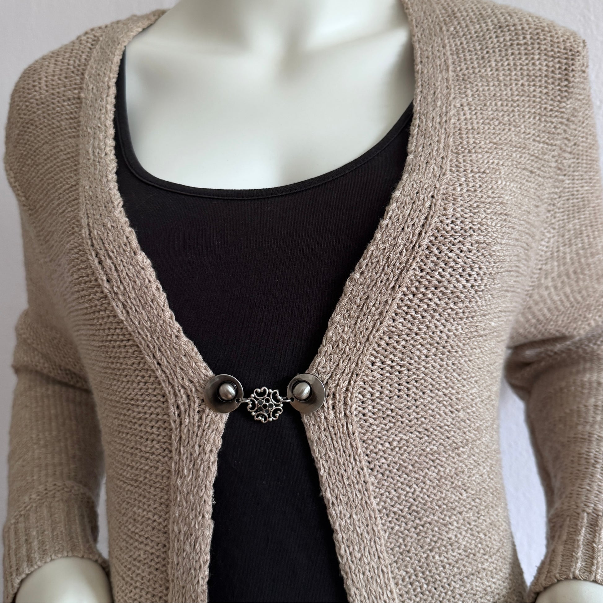 Vestsluiting Barokbloei in zachte grijstinten, gedragen op een open gebreid vest met rustige, klassieke uitstraling.