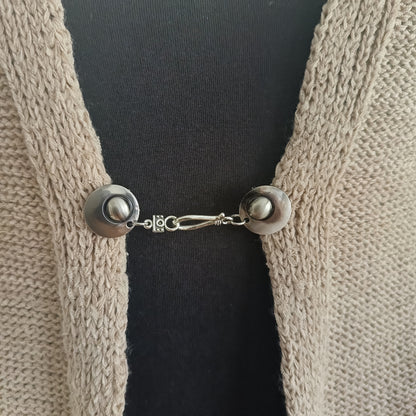 Zilverkleurige vestsluiting De Classic met haak-en-oogsluiting, rustig en tijdloos op een open gebreid vest.