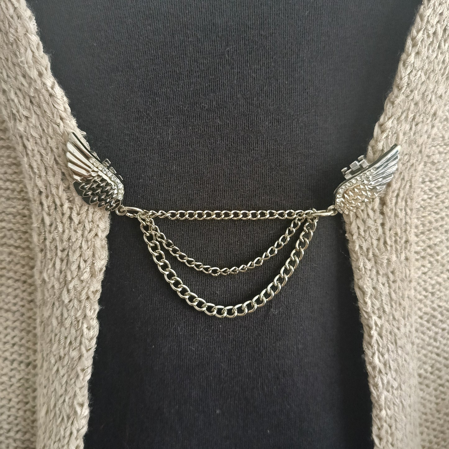 Close-up van een zilverkleurige vestsluiting met verfijnde vleugels en drie elegant vallende kettingen, die vrijheid en balans uitstralen.