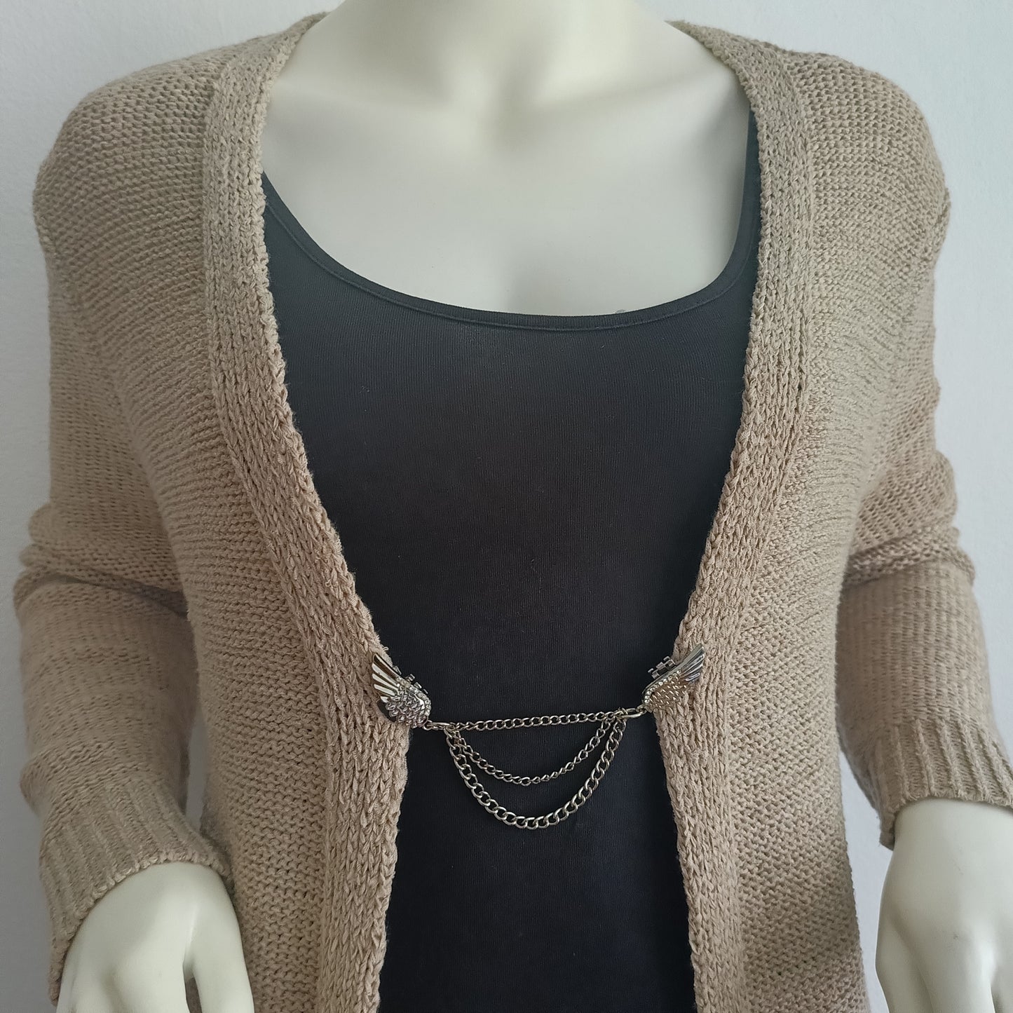 Zilverkleurige vestsluiting met sierlijke vleugels en drie kettingen, gedragen op een open vest voor een elegant en krachtig accent.