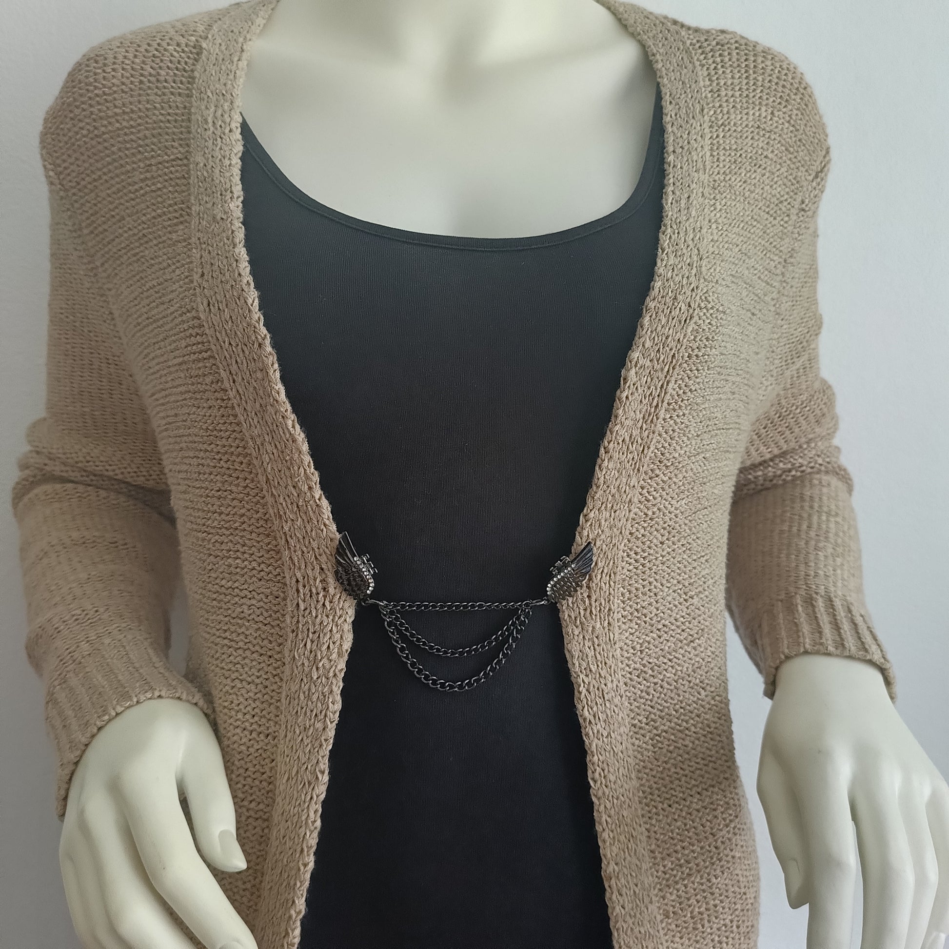 Zwartkleurige vestsluiting met gevleugelde details en drie sierlijke kettingen, gedragen op een vest voor een krachtige en elegante uitstraling.