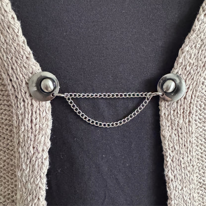 Vestsluiting De Keten in zilverkleur met twee sierlijke kettingen, geeft een rustige en elegante sluiting van een vest.