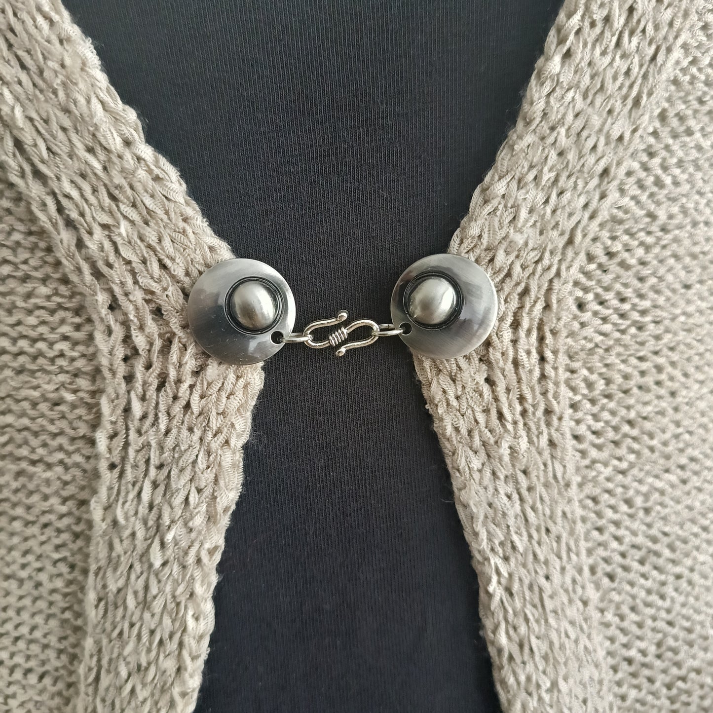 Zilverkleurige haak-en-oog vestsluiting ‘De Twist’ met ronde metalen eindstukken, elegant bevestigd op een neutrale ondergrond.