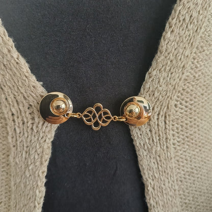 Deze gouden vestsluiting straalt verbondenheid en zachtheid uit. Een sierlijk symbool van evenwicht, met een warme glans.