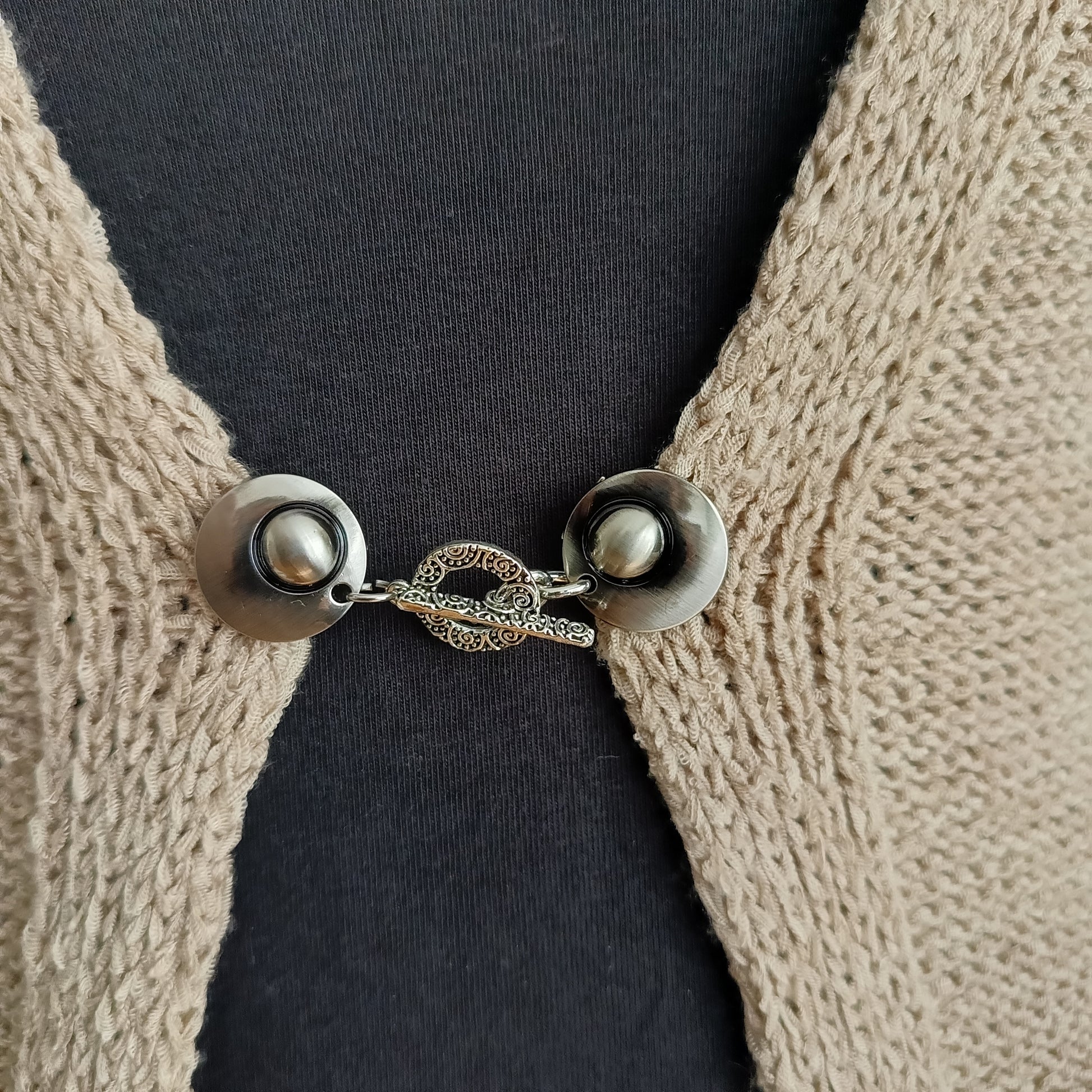 Close-up van een zilverkleurige vestsluiting met een verfijnde Arabesque-bedel, handgemaakt voor een elegante en sierlijke uitstraling.