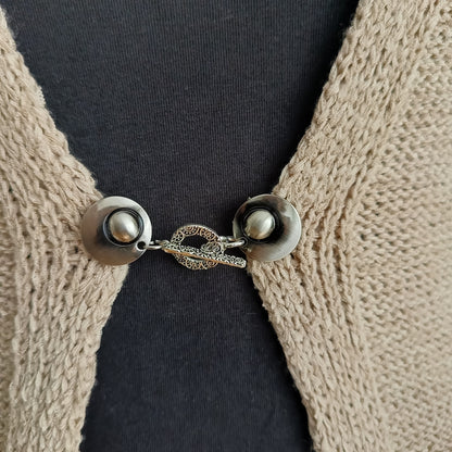 Close-up van een zilverkleurige vestsluiting met een verfijnde Arabesque-bedel, handgemaakt voor een elegante en sierlijke uitstraling.