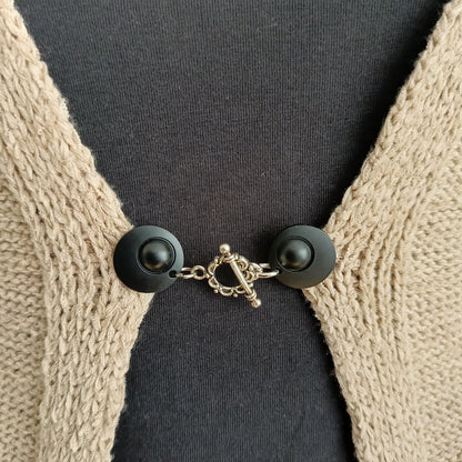 Vestsluiting met mat zwarte clips en een zilverkleurige bloemrand-bedel, handgemaakt voor een elegante en moderne uitstraling.