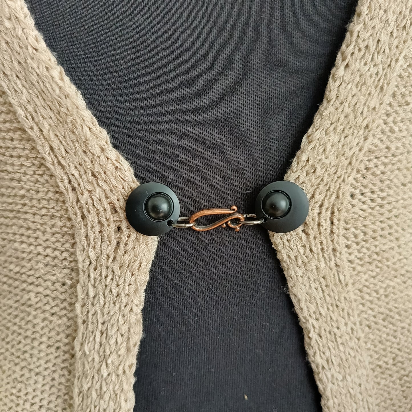 Vestsluiting met mat zwarte clips en een koperkleurige haak-en-oog sluiting, handgemaakt voor een warme en stijlvolle uitstraling.
