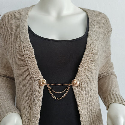 Goudkleurige vestsluiting met drie fijne kettingen, die elke outfit een elegante en stijlvolle afwerking geeft.