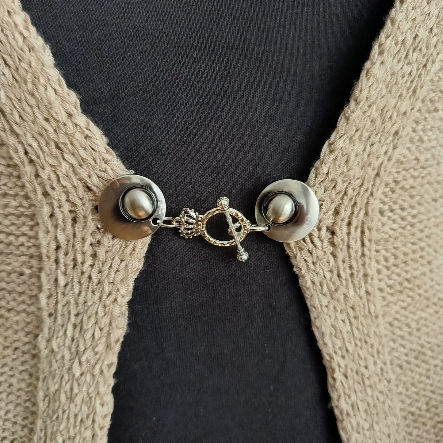 Close-up van een zilverkleurige vestsluiting met een verfijnde kroonbedel, handgemaakt voor een elegante en vorstelijke uitstraling.