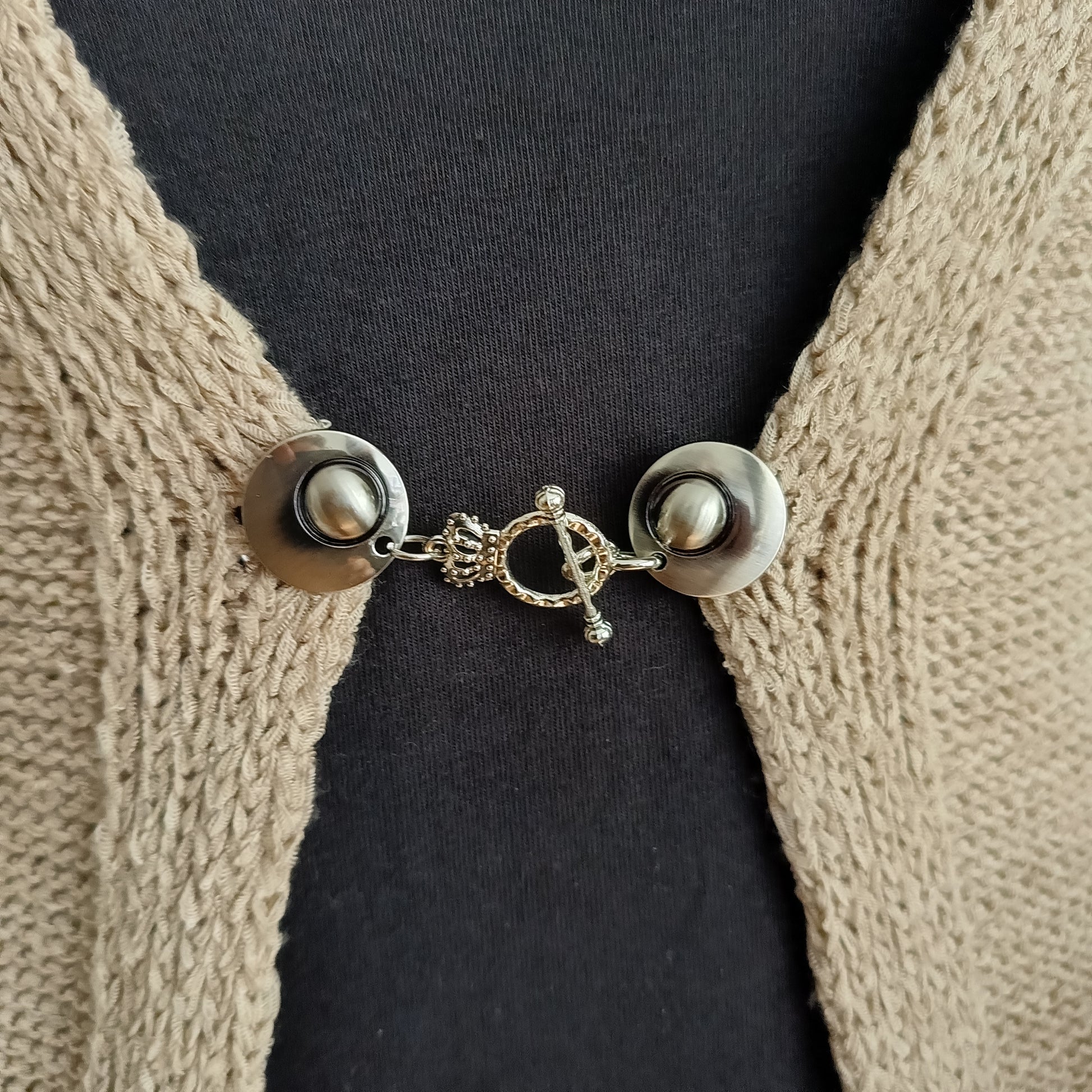 Close-up van een zilverkleurige vestsluiting met een verfijnde kroonbedel, handgemaakt voor een elegante en vorstelijke uitstraling.