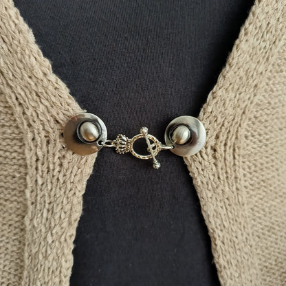 Close-up van een zilverkleurige vestsluiting met een verfijnde kroonbedel, handgemaakt voor een elegante en vorstelijke uitstraling.