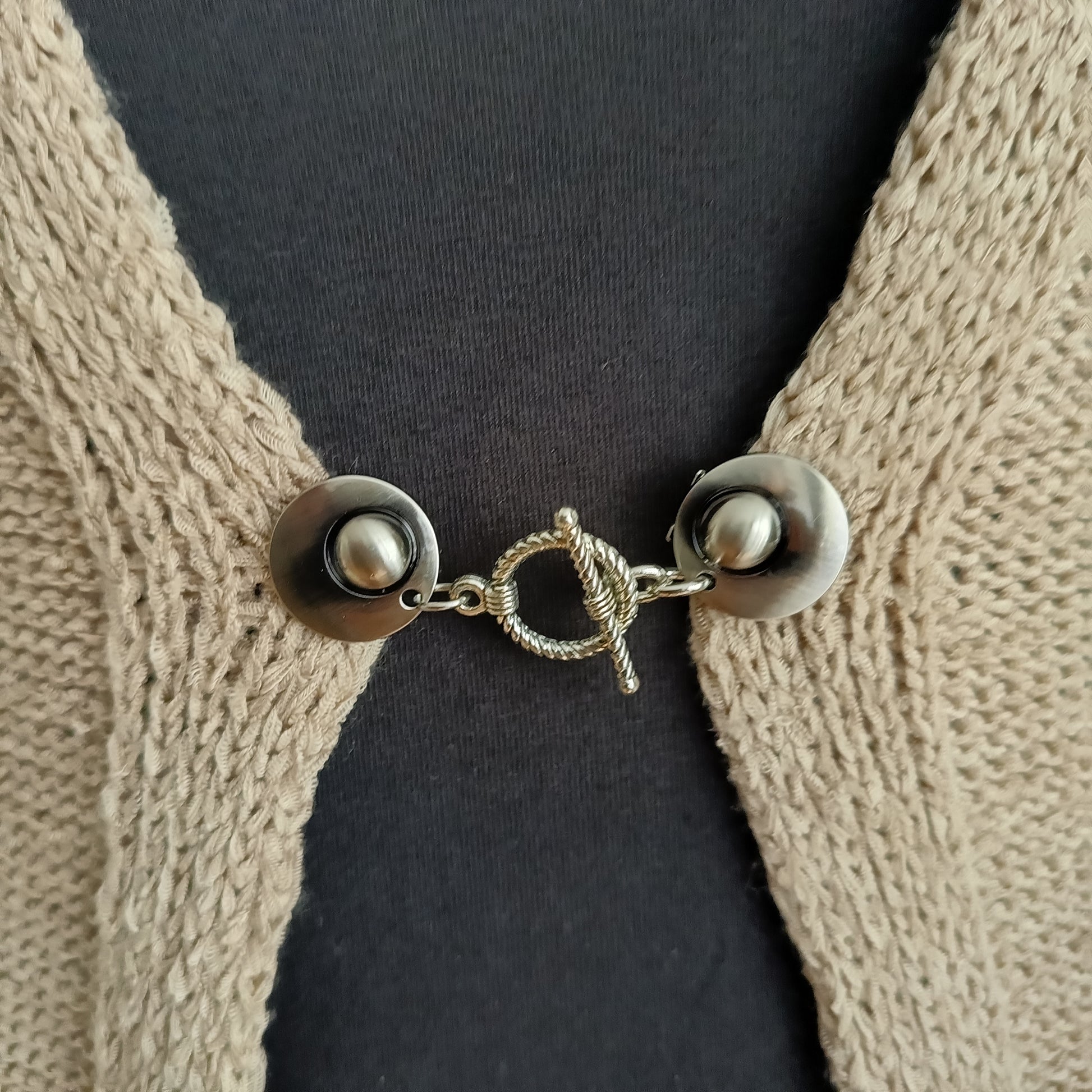 Close-up van een zilverkleurige vestsluiting met een sierlijke spiraalvormige T-Bar, handgemaakt voor een elegante en verfijnde uitstraling.