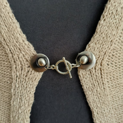 Close-up van een zilverkleurige vestsluiting met een sierlijke spiraalvormige T-Bar, handgemaakt voor een elegante en verfijnde uitstraling.