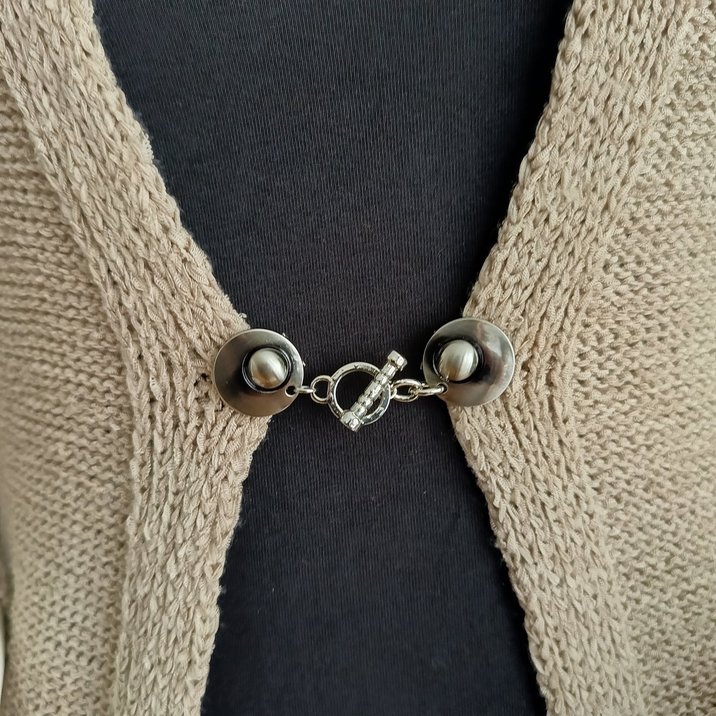 Close-up van een zilverkleurige vestsluiting met een verfijnde ritme-bedel, handgemaakt voor een elegante en tijdloze uitstraling.