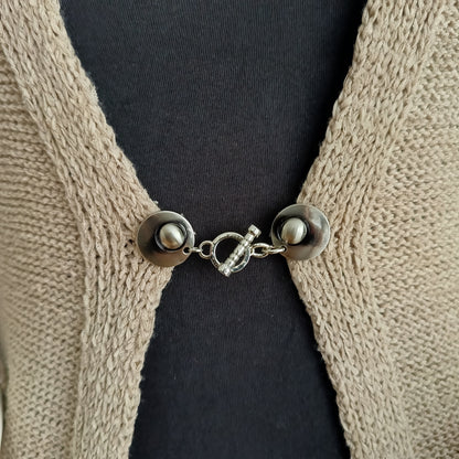 Close-up van een zilverkleurige vestsluiting met een verfijnde ritme-bedel, handgemaakt voor een elegante en tijdloze uitstraling.