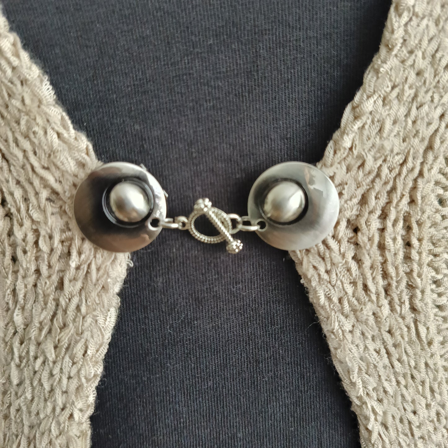 Close-up van een zilverkleurige vestsluiting met een verfijnde verbonden-bedel, handgemaakt voor een elegante en betekenisvolle uitstraling.