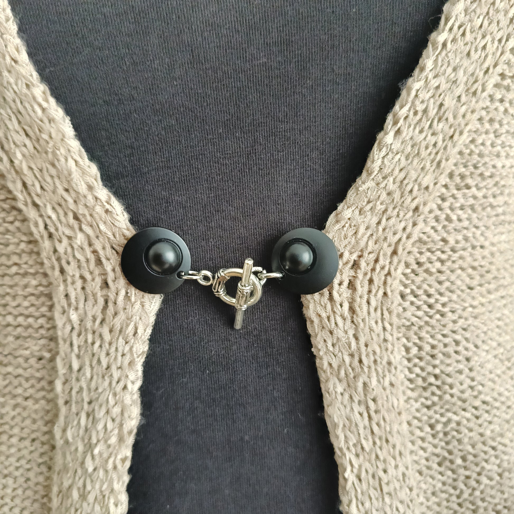 Vestsluiting met mat zwarte clips en een zilverkleurige evenwichtsbedel, handgemaakt voor een stijlvolle en harmonieuze uitstraling.