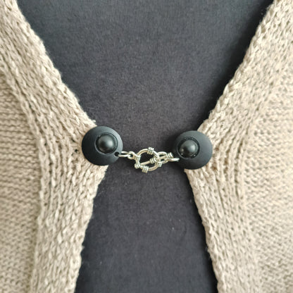 Close-up van een vestsluiting met mat zwarte clips en een zilverkleurige structuurbedel, handgemaakt voor een krachtige en elegante uitstraling.