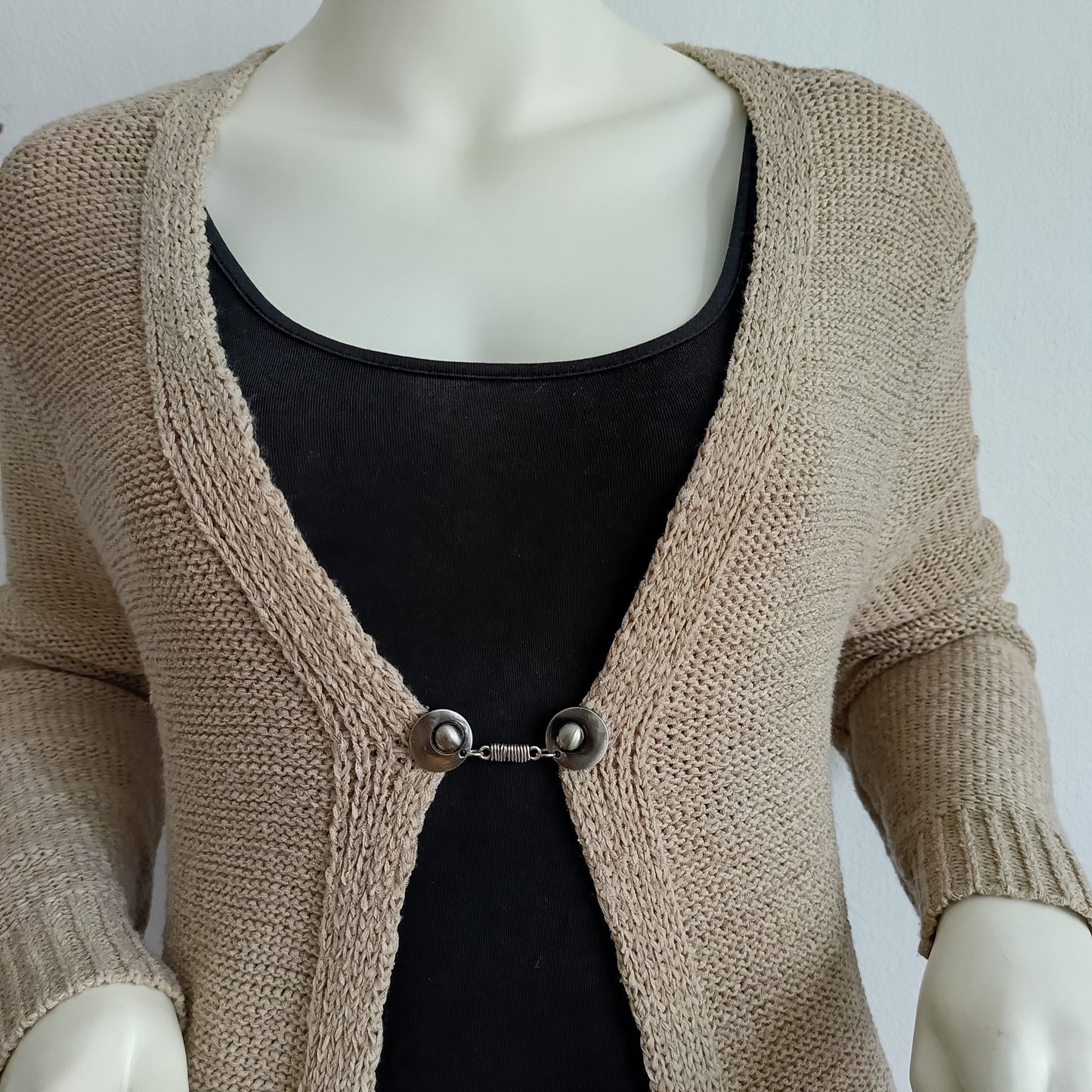 “Handgemaakte zilveren vestclip met wikkelvormig middenstuk, bevestigd op een gebreid vest voor een elegante en stevige sluiting.”