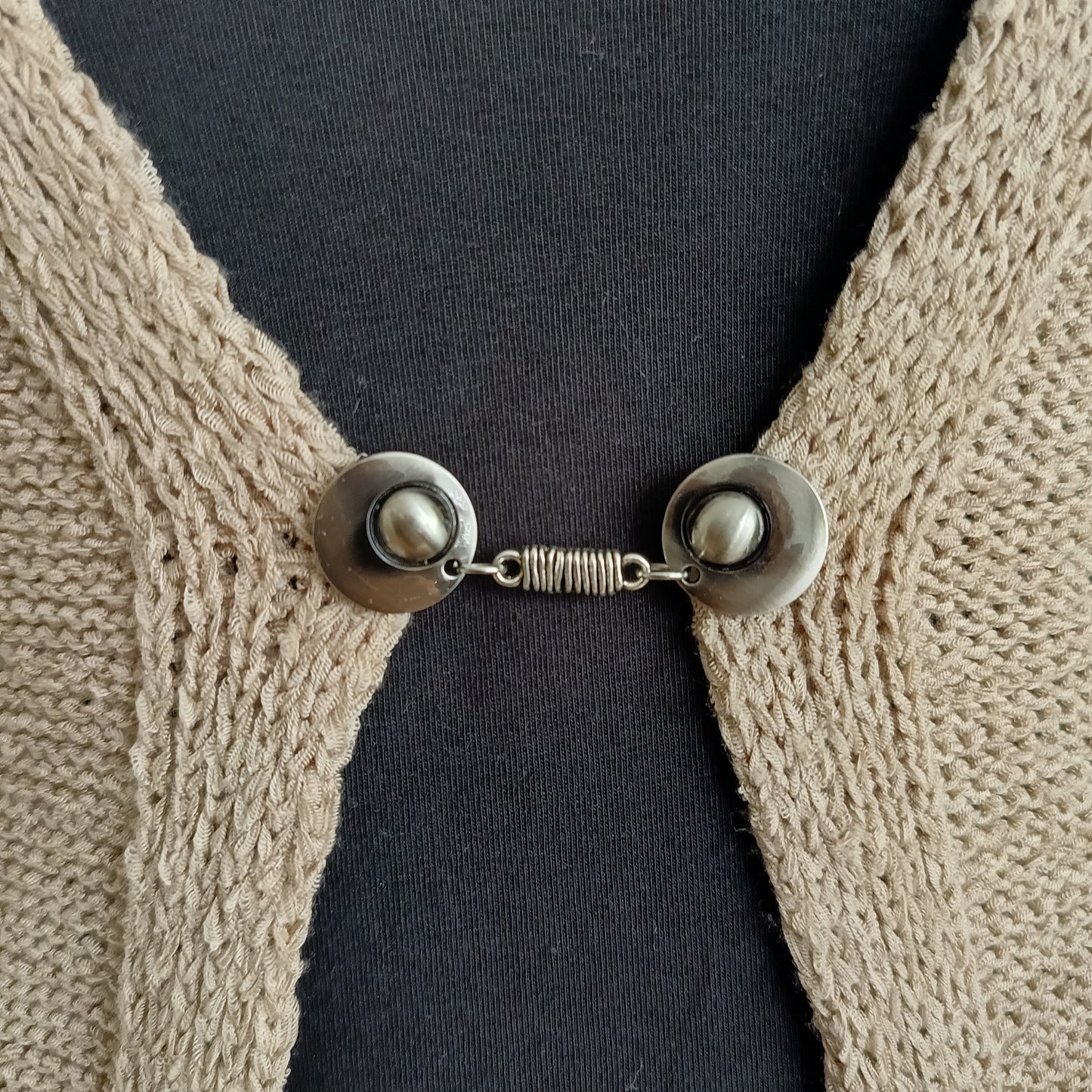 “Zilverkleurige vestsluiting met verfijnde wikkelvorm, handgemaakt en stevig bevestigd op een vest.”