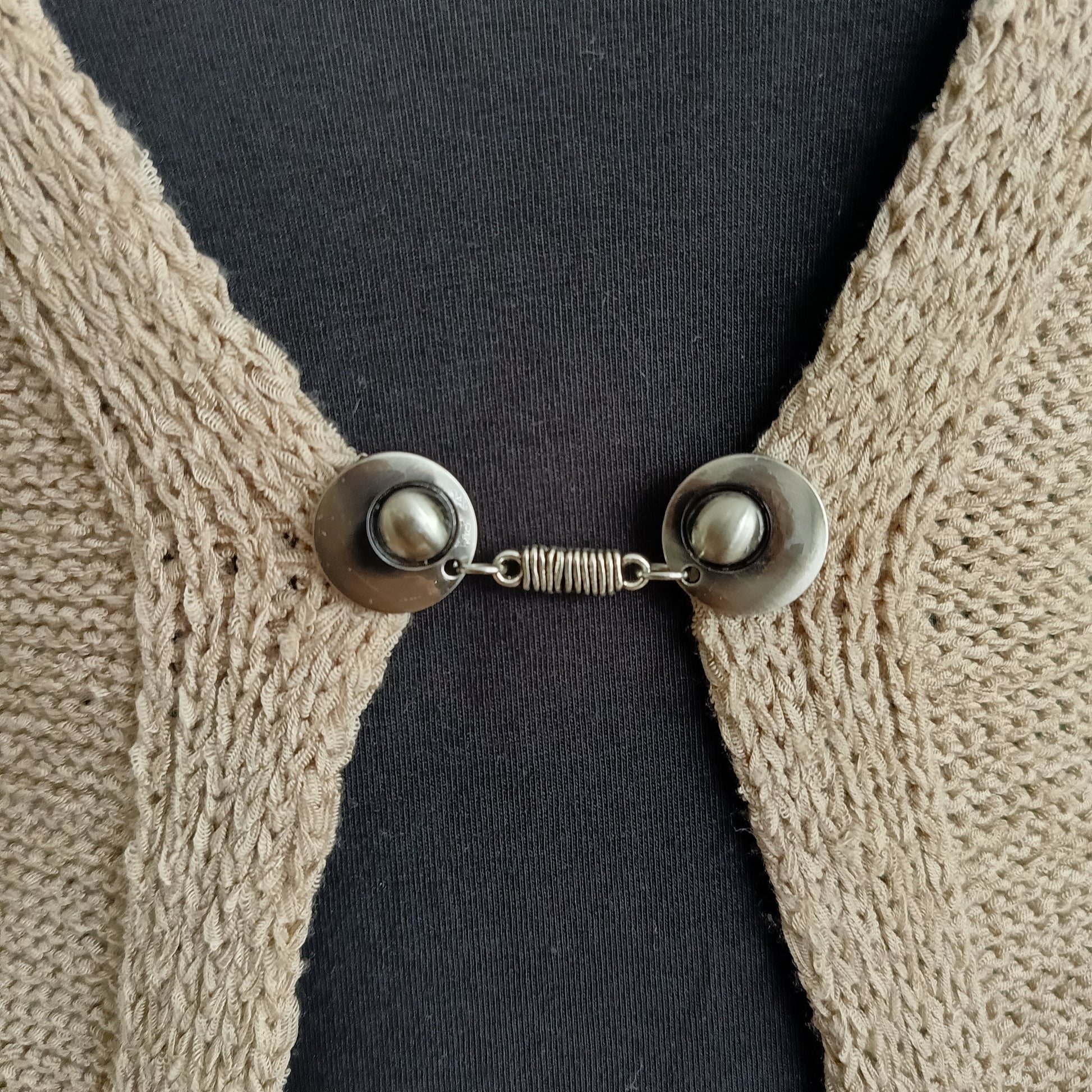 “Zilverkleurige vestsluiting met verfijnde wikkelvorm, handgemaakt en stevig bevestigd op een vest.”