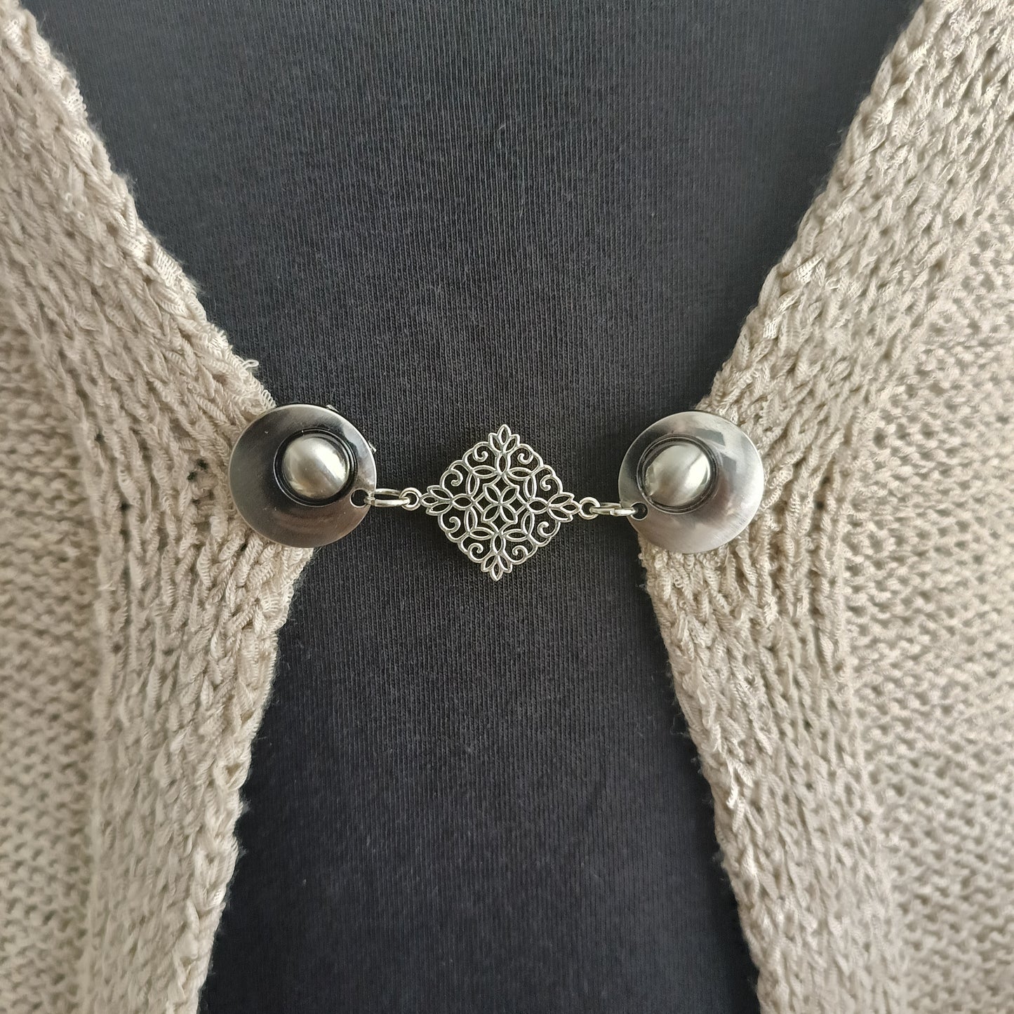 Zilverkleurige vestsluiting Decoratie met filigraan diamantvorm, bevestigd aan een beige vest.