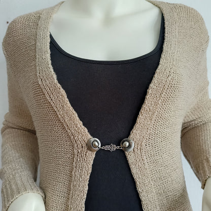 “Zilverkleurige Fatima-hand vestsluiting op een beige gebreid vest, handgemaakt en stevig voor dagelijks gebruik.”