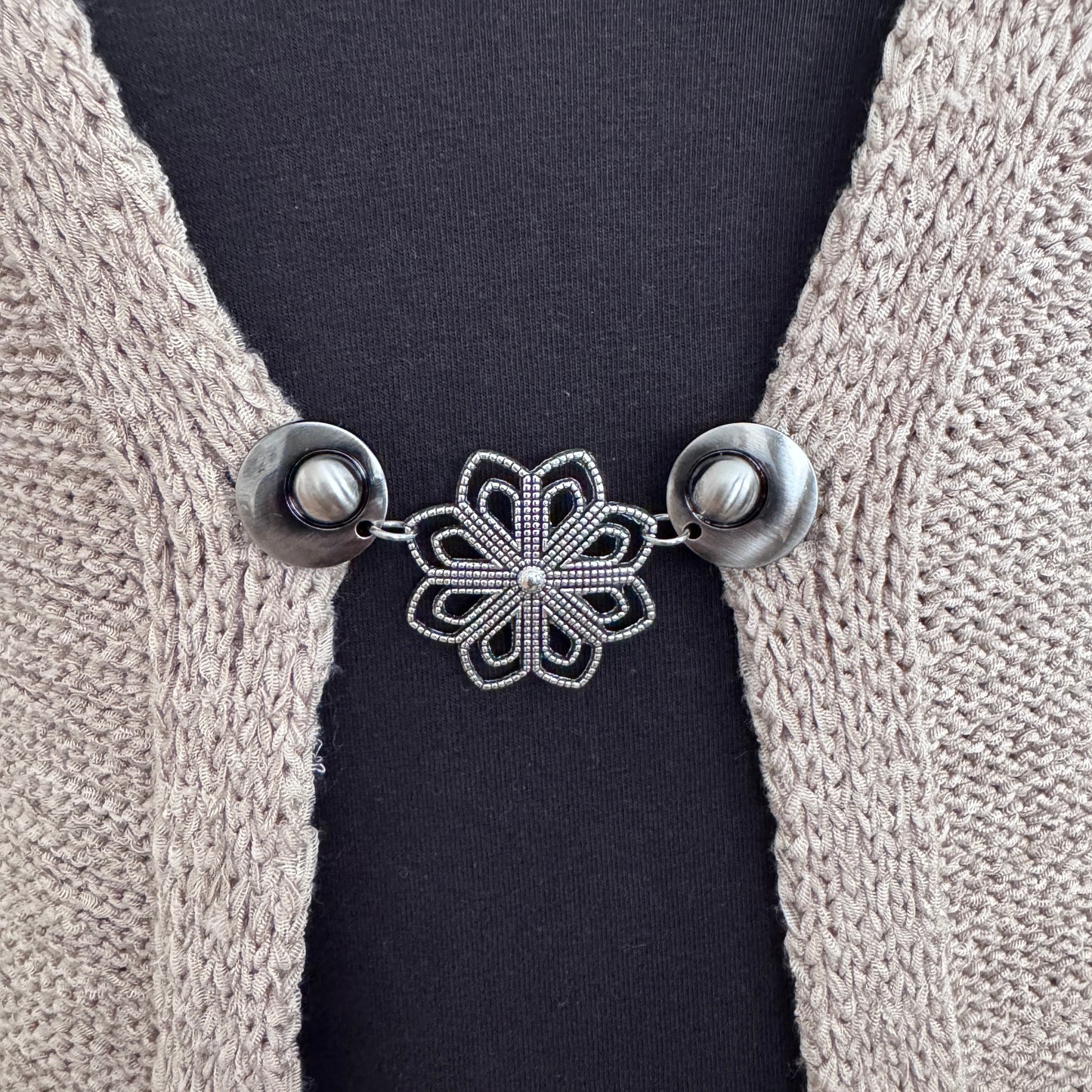 Handgemaakte zilverkleurige vestsluiting Ijsbloem van Fashionclip met opengewerkt bloemmotief op een beige vest.